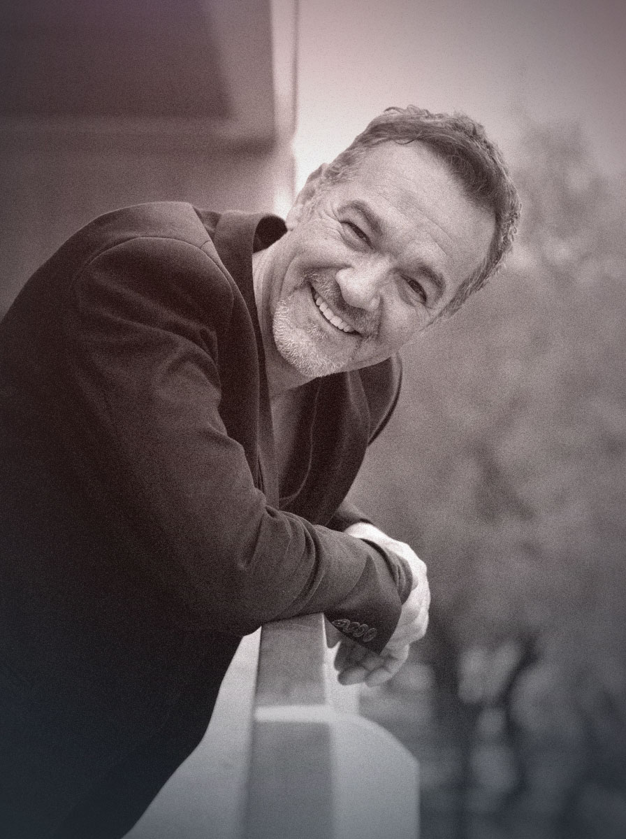 Black-and-white portrait of Joe R. Vasquez leaning on a rail, smiling